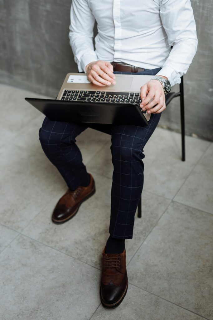 Businessman in white shirt working on laptop while seated indoors. Focus on attire and technology.